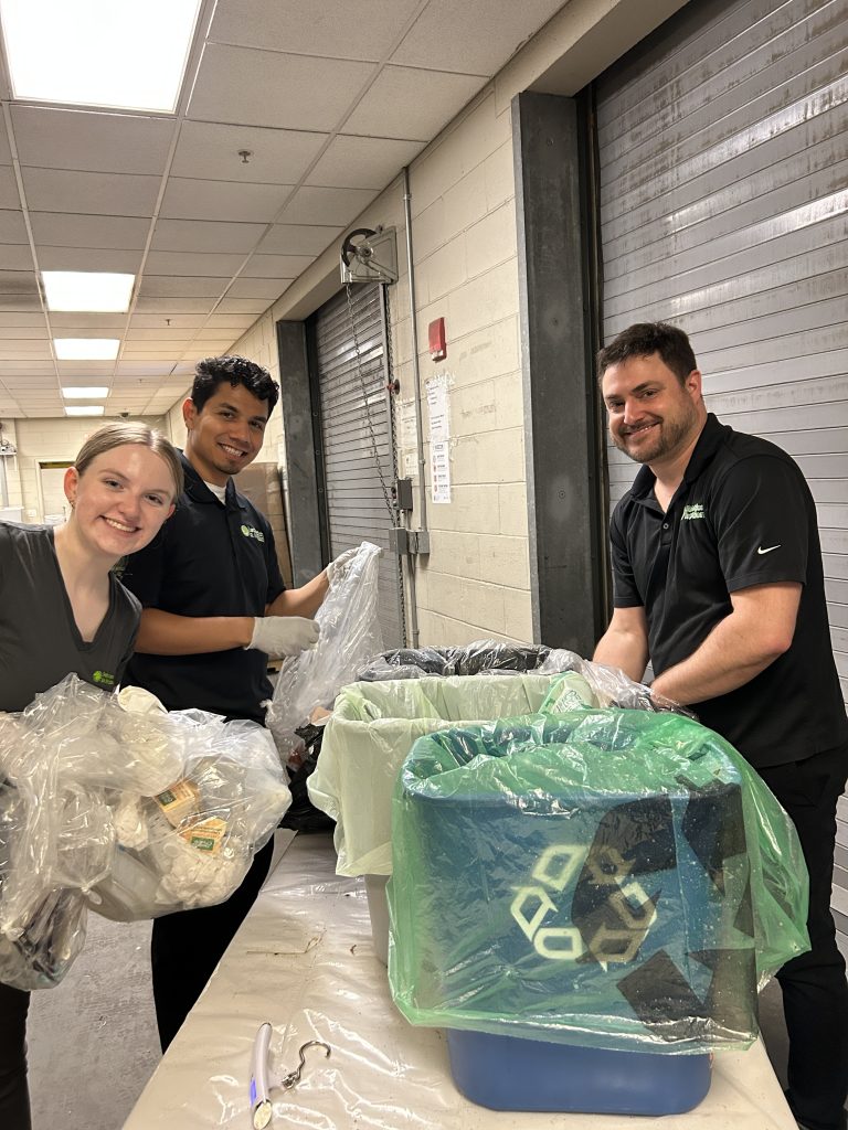 Group of three happy people sorting waste between recycling, compost, and trash.