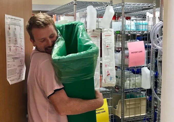 Nurse in hospital setting excitedly hugging a green recycle bin.