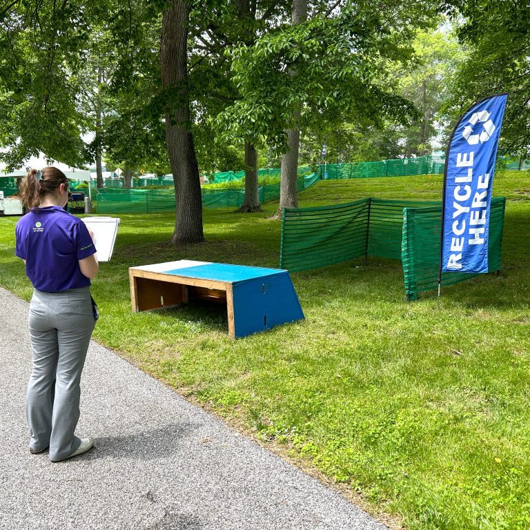 Reduction In Motion employee assessing waste stations at an outdoor event for ideal waste and recycling setup.